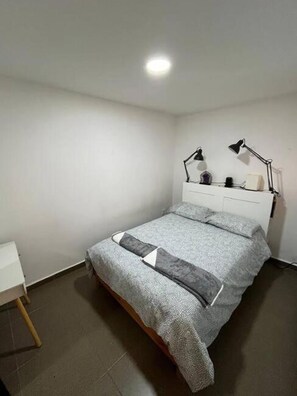 Un dormitorio con una cama, dos lámparas de noche, una mesita de noche y una pequeña mesa.