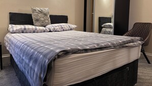 A neatly made bed with a striped bedspread, two pillows, and a headboard. There are wall-mounted lights and a large mirror on the wall. - The Lansbury - Whitby  (Whitby)