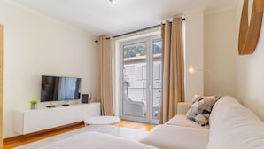 A modern living room with a sofa, a TV, a small round table, and a sliding glass door leading to an outdoor area. - Cozy Santa Cruz (Santa Cruz)