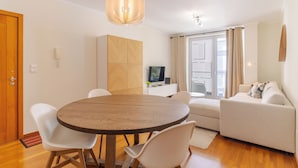 A modern living room with a round wooden dining table, white chairs, a beige sofa, and a television on a white cabinet. - Cozy Santa Cruz (Santa Cruz)