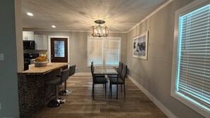 A modern kitchen with a built-in microwave, a wooden island with bar stools, and a dining area with a table and chairs.