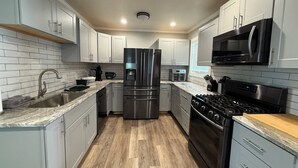 A modern kitchen with stainless steel appliances, white cabinetry, and a wooden floor.
