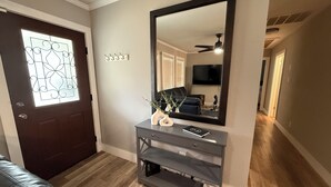 A hallway with a dark brown door, a mirror, a small table with a vase and a book, and a wooden floor.