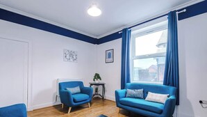 A living room with two blue sofas, a small table with a plant, and a large window with blue curtains.