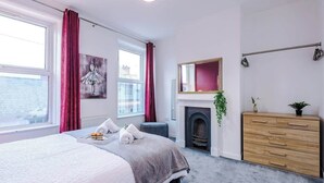 A bedroom with a bed, a dresser, a fireplace, and a window with curtains.