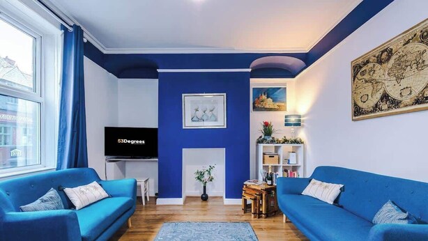 A living room with two blue sofas, a flat-screen TV, a world map on the wall, and a small table with a vase of flowers.