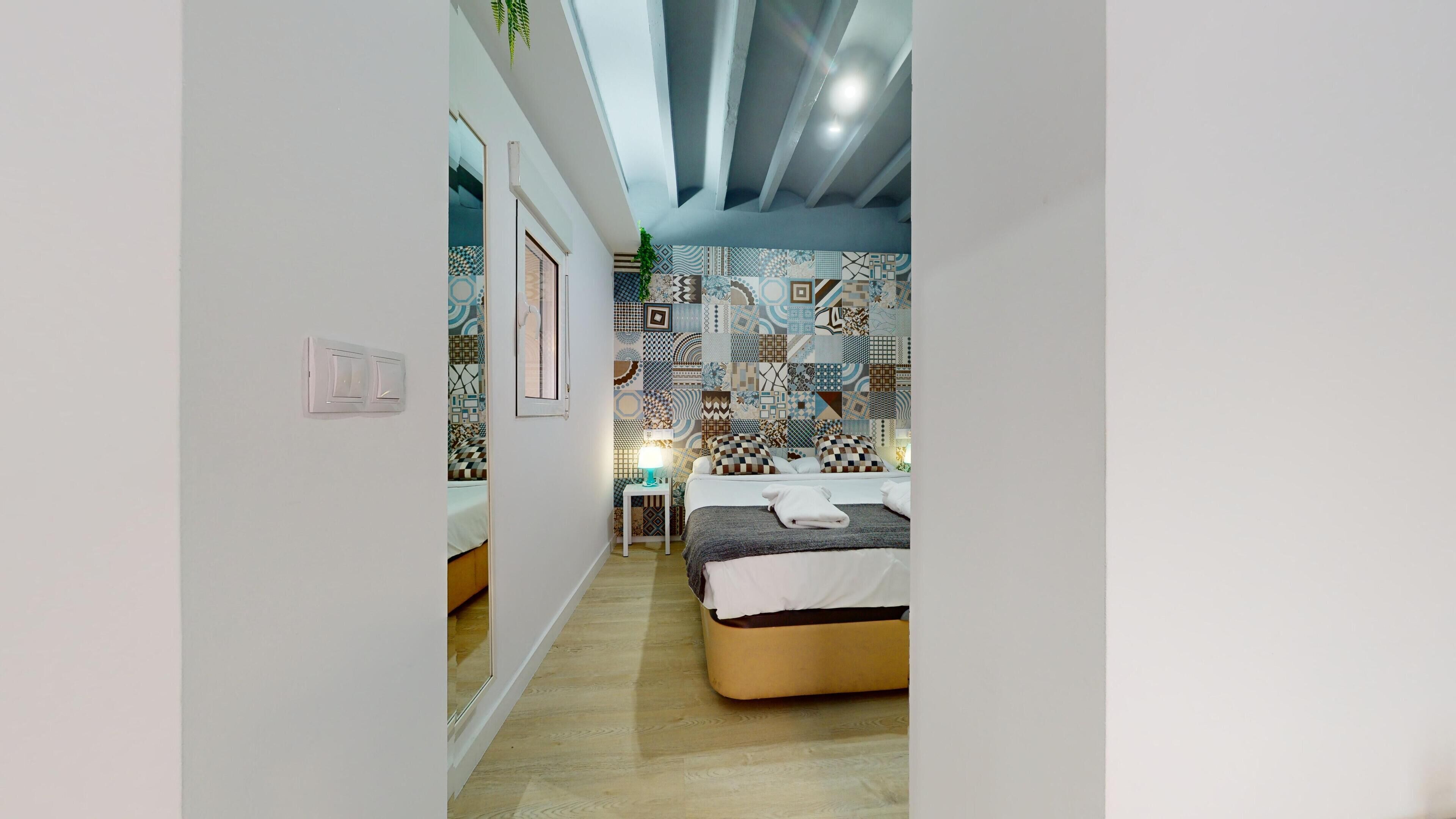 Un dormitorio moderno con pared estampada, una cama con edredón blanco y una mesita de noche con lámpara.