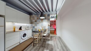 A modern kitchen with a washing machine, a dining area with stools, and a patterned wall.