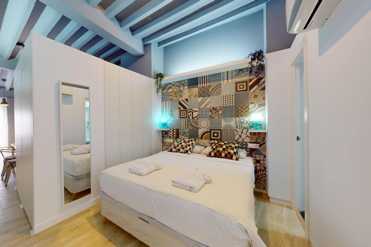 Een moderne slaapkamer met een groot bed, een spiegel en een bekleder met patroon.