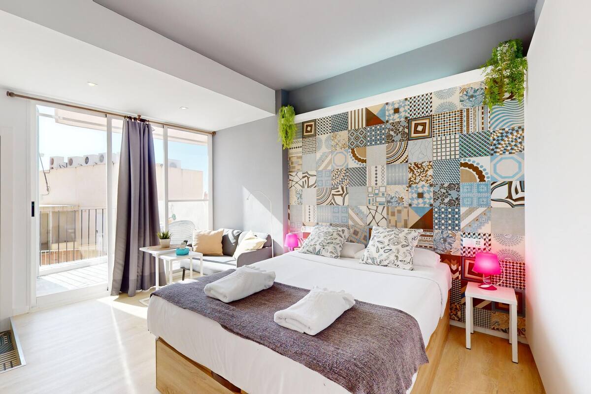 Een moderne slaapkamer met een groot bed, een klein bureau, een balkon en een behang met een patroon.