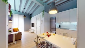 A modern kitchen with white cabinets, a stainless steel refrigerator, and a dining area with a white table and chairs.