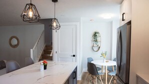 A modern kitchen with a marble countertop, a dining area with a round table and chairs, and a built-in refrigerator.
