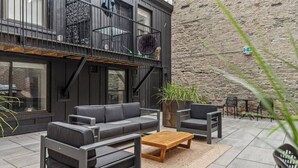 Un espace extérieur aménagé avec un canapé, des fauteuils et une table, le tout adossé à un mur en pierre.