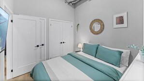 Une chambre à coucher avec un lit, deux portes blanches, un miroir rond et un tableau encadré au mur.