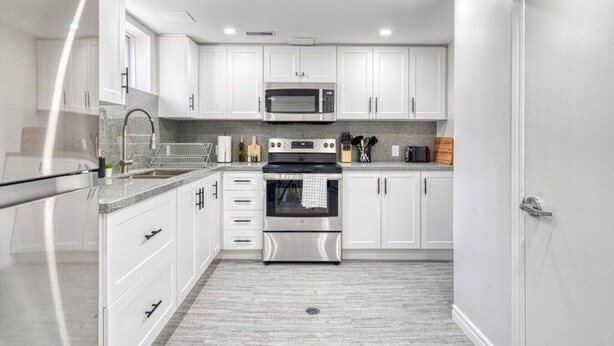 A modern kitchen with white cabinets, stainless steel appliances, and a granite countertop.