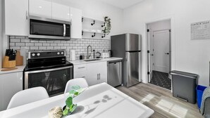 Una cocina moderna con armarios blancos, un microondas, horno y refrigerador de acero inoxidable. Hay un lavamanos, un escurreplatos y una pequeña planta en maceta.