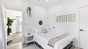Un dormitorio minimalista con una cama grande, mesitas de noche, una planta colgante y cuadros en la pared.