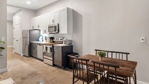 A modern kitchen with grey cabinets, a microwave, a refrigerator, and a dining area with a wooden table and chairs. - 1Bedroom | Downtown | Gym & Coworking space + Wifi (Cincinnati)