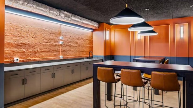A modern kitchen with a brick wall backsplash, a long countertop, and bar stools. - 1Bedroom | Downtown | Gym & Coworking space + Wifi (Cincinnati)