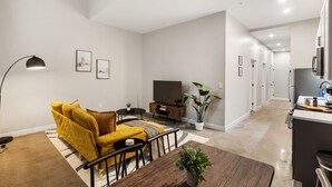 A modern living room with a sofa, TV, and dining area. A kitchen is visible in the background. - 1Bedroom | Downtown | Gym & Coworking space + Wifi (Cincinnati)