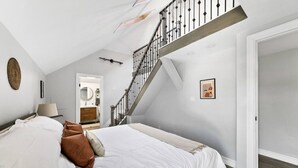 A bedroom with a large bed, a staircase, and a bathroom visible through an open door.