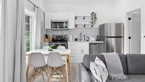 A modern kitchen with white cabinets, a stainless steel refrigerator, and a dining area with a table and chairs.