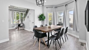 A modern dining area with a wooden table and black chairs, a potted plant, and large windows with curtains.