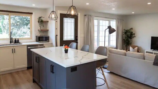 A modern kitchen with a central island, a dining area with a sofa, and a TV. - 5Bd/2Ba Luxe Family Home - WIFI, Parking (Kitchener)