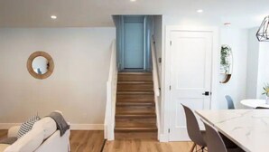A modern interior with a staircase leading to a door, a dining area with a marble table, and a white sofa. - 5Bd/2Ba Luxe Family Home - WIFI, Parking (Kitchener)