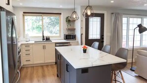 A modern kitchen with a central island, white cabinets, and a large window providing natural light. - 5Bd/2Ba Luxe Family Home - WIFI, Parking (Kitchener)