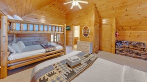 Une chambre dans une cabane en bois, avec des lits superposés, une commode, un miroir et un ventilateur de plafond.