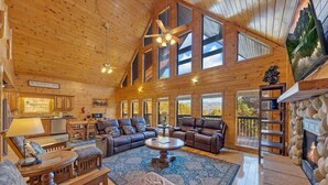 Un intérieur spacieux de chalet en bois, avec un grand salon, de nombreux espaces pour s’asseoir et une cheminée.