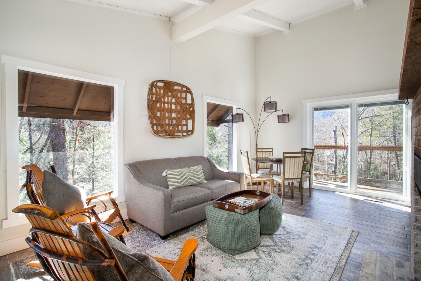 A spacious living area with a grey sofa, wooden chairs, a woven wall hanging, and a dining set.