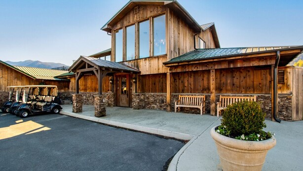 A rustic wooden building with large windows, stone pillars, and a covered area with benches. - Peaceful Heights with Cozy Decks and Smart TV! (Townsend)