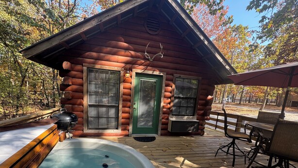 A log cabin with a hot tub, outdoor seating, and a deck.