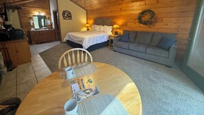 A cozy cabin with a wooden interior, a bed, a sofa, a dining table with a chair, and a ceiling fan.