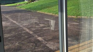 Vista pela janela de um edifício, com área pavimentada em frente, um deck de madeira e uma grande casa com torre ao fundo.