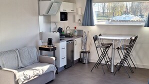 Quarto compacto e moderno com cozinha compacta, sofá, mesa de jantar com cadeiras e cama.