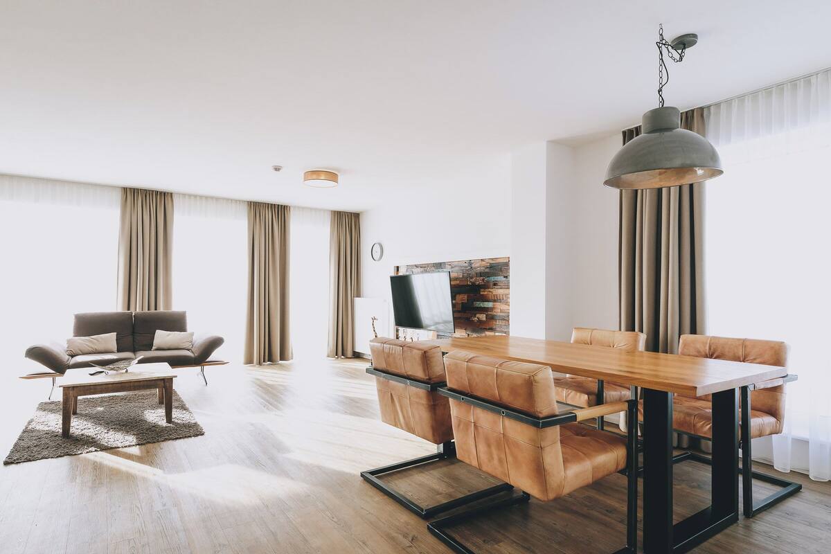 Un salon spacieux avec une table à manger en bois, des canapés en cuir et un grand luminaire suspendu.