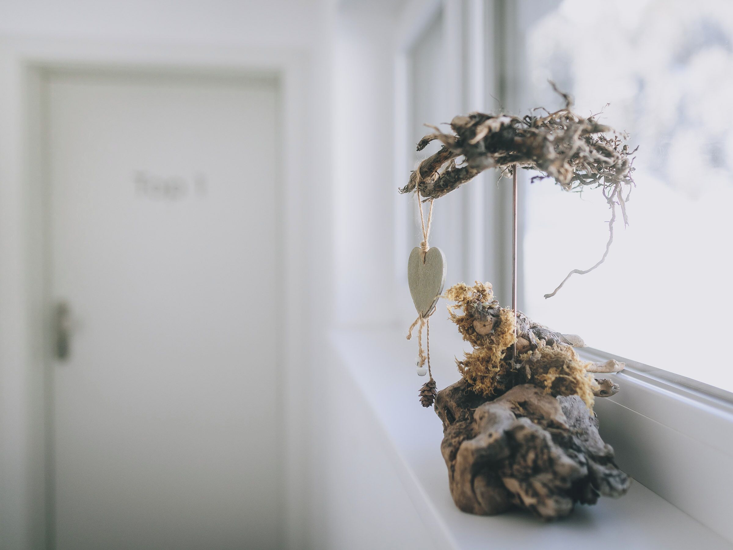 A rustic decor piece with a heart-shaped ornament and dried branches on a windowsill.