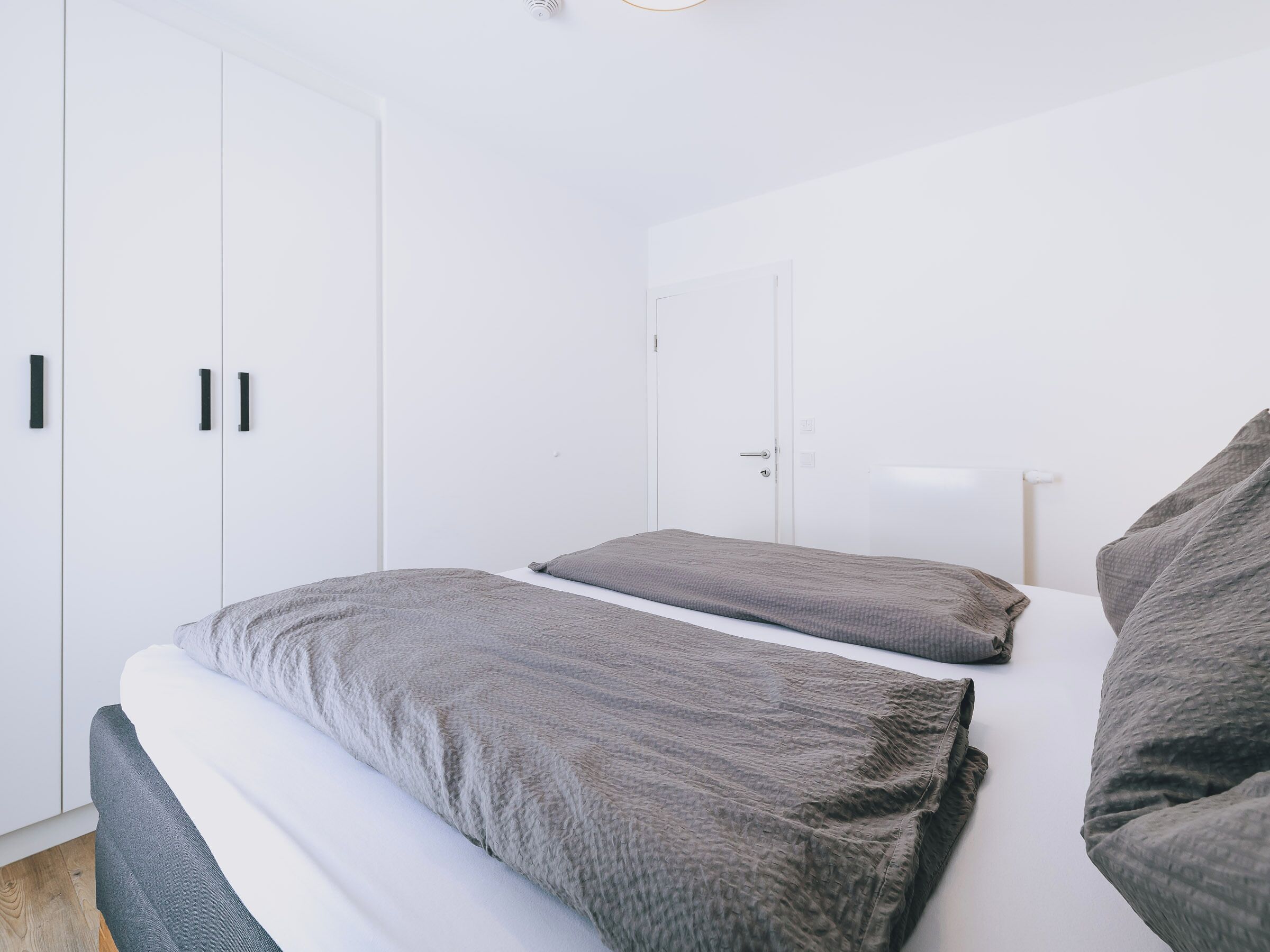 A minimalist bedroom with two beds, white walls, and a wardrobe.