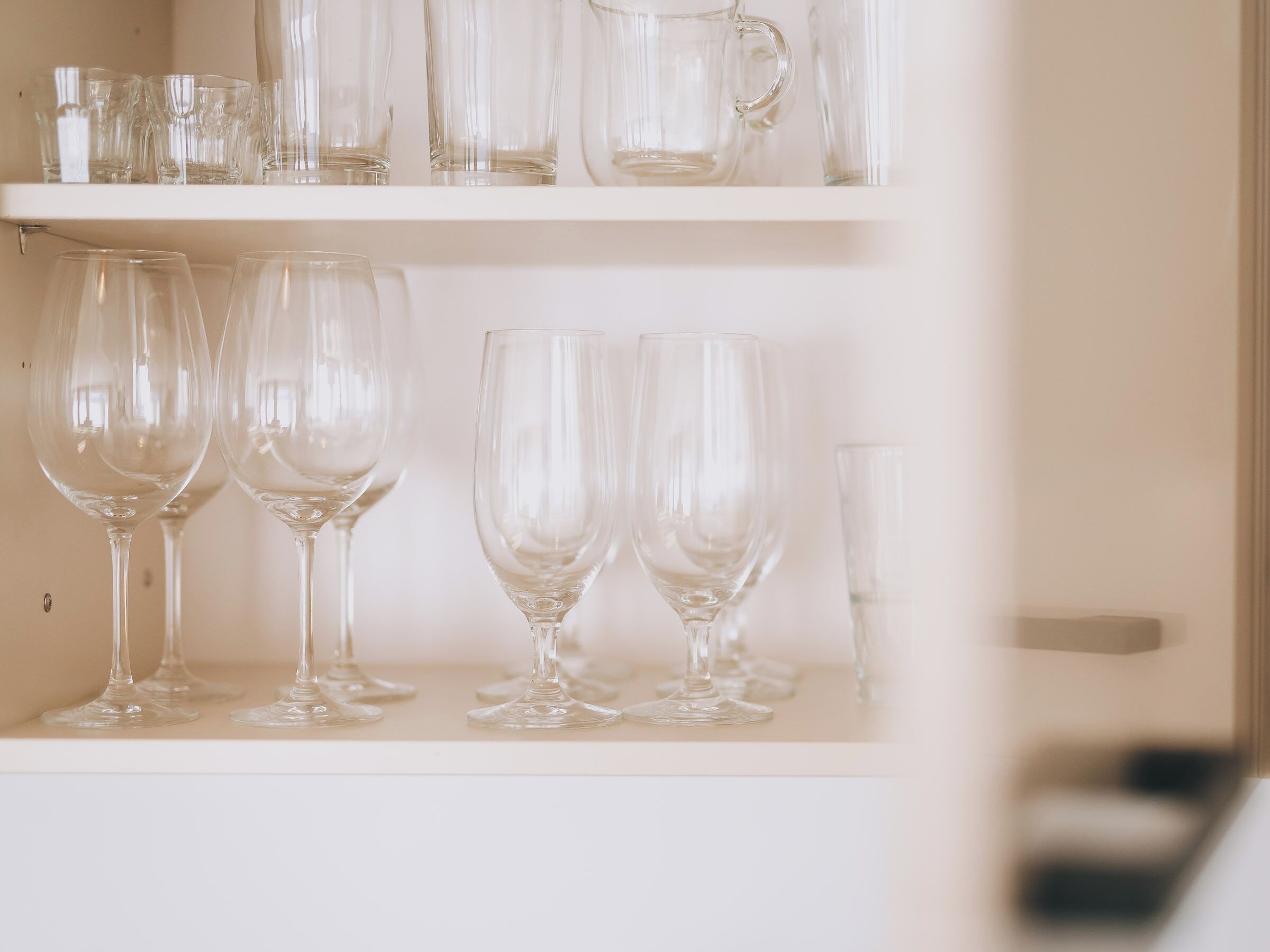 A shelf with various glassware including wine glasses and a pitcher.