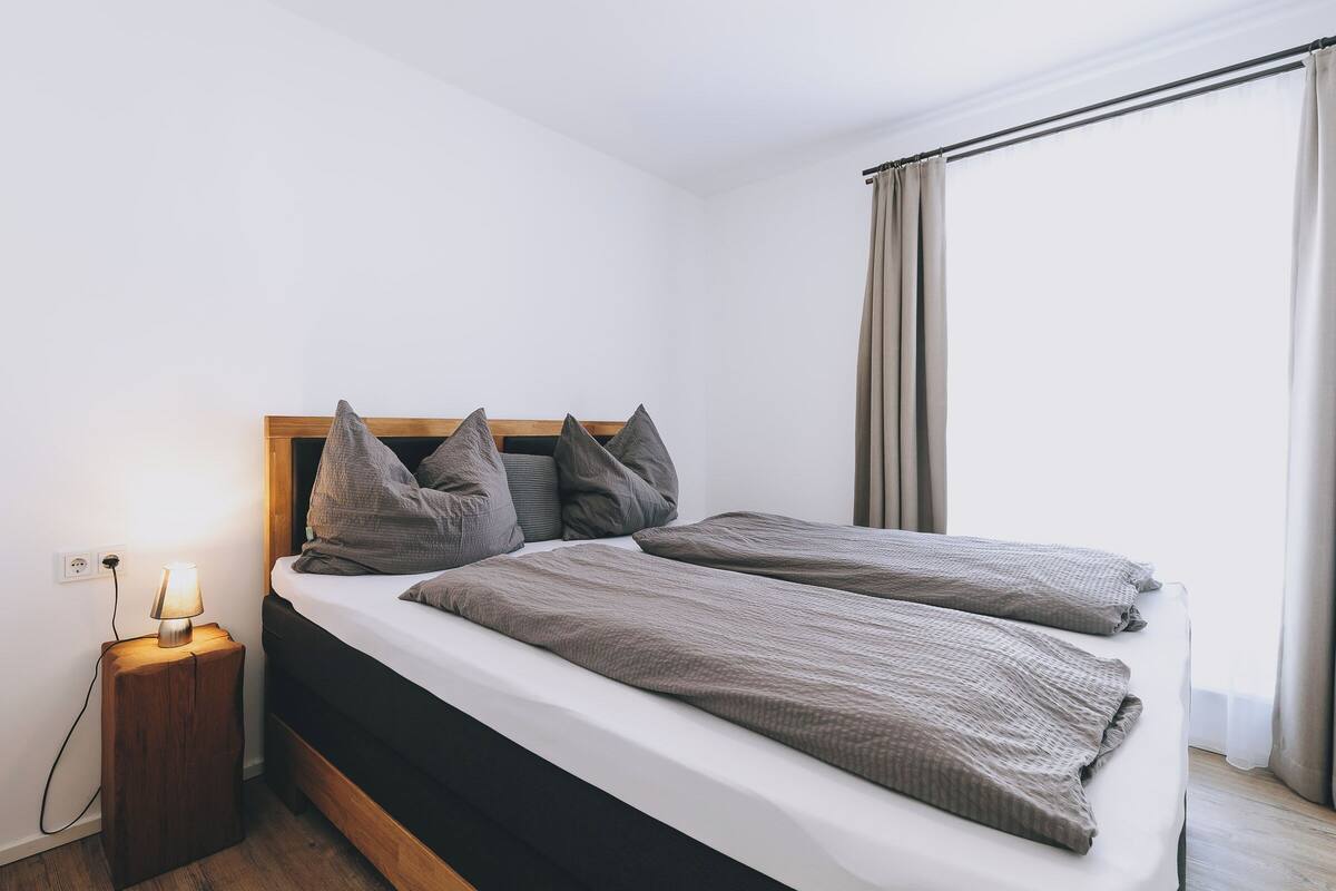 Un lit double avec une tête de lit en bois, une literie grise et une lampe de chevet.
