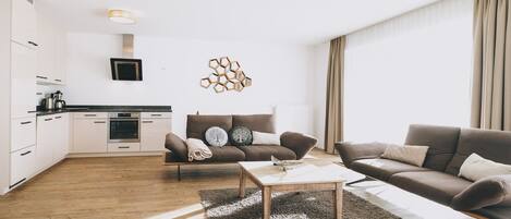 A modern living room with a sofa, coffee table, and a kitchen area with cabinets and appliances.