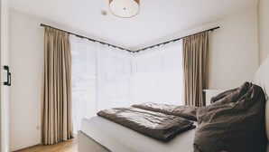 Un dormitorio moderno con una cama grande, una lámpara de noche y vistas a la ciudad a través de amplios ventanales.
