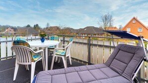 A balcony with a cushioned chair, a table, and chairs with colorful cushions. - Gemutliche Ferienwohnung in Tating (Tating)