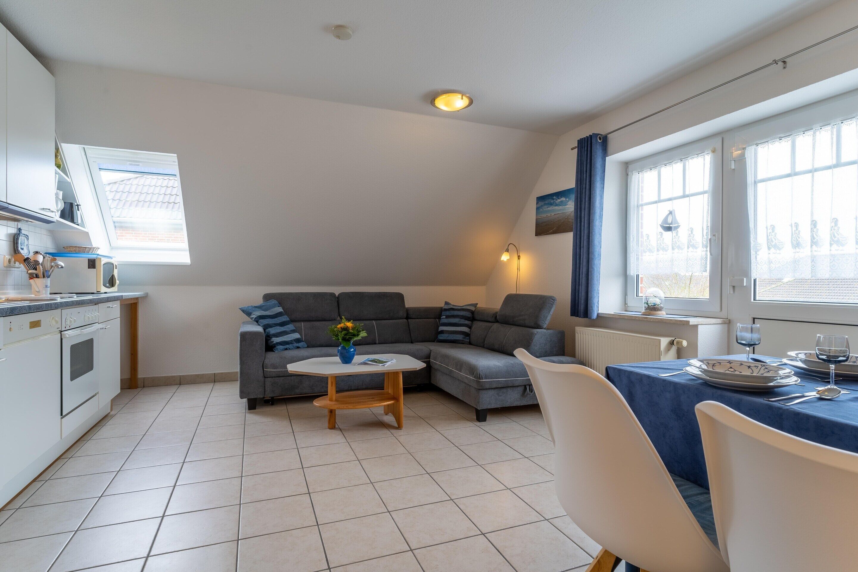 A modern kitchen with a dining area, a gray sectional sofa, and a small round table with a vase.