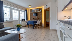 A modern kitchen with white cabinets, a built-in oven, and a dining area with a table and chairs. - Gemutliche Ferienwohnung in Tating (Tating)
