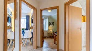 A corridor leading to a dining area with a table and chairs, a bed, and a window with curtains. - Gemutliche Ferienwohnung in Tating (Tating)