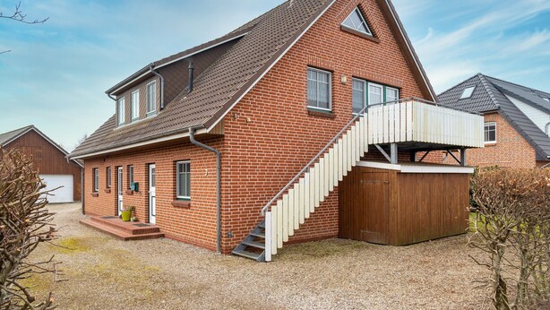 A two-story brick house with a sloped roof, a wooden staircase, and a small porch area. - Gemutliche Ferienwohnung in Tating (Tating)